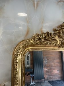 An image showing the corner of a large gold ornate mirror with scrolls and flowers in Atelier hairdressers